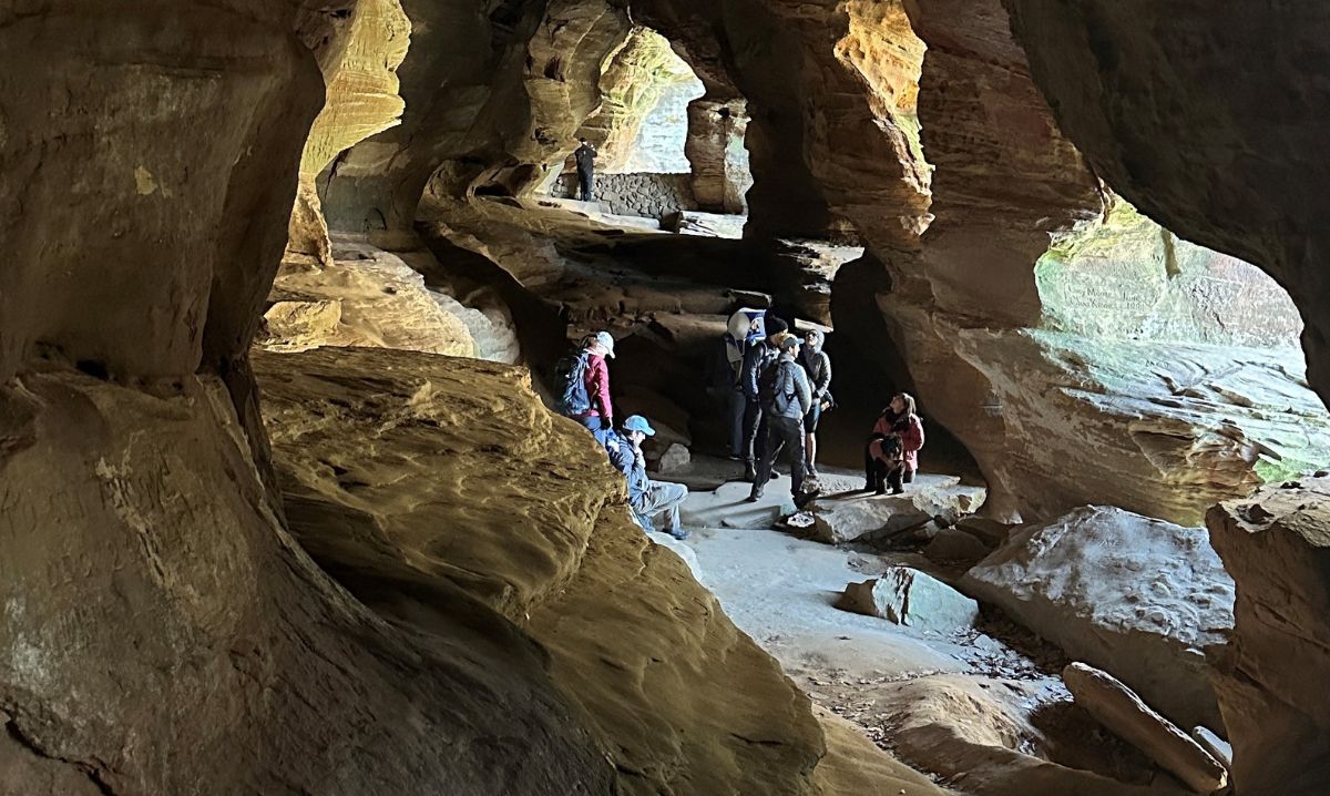 A group of hikers explores the scenic Old Man's Cave in Hocking Hills, Ohio, surrounded by stunning rock formations and natural light filtering through the cave openings.