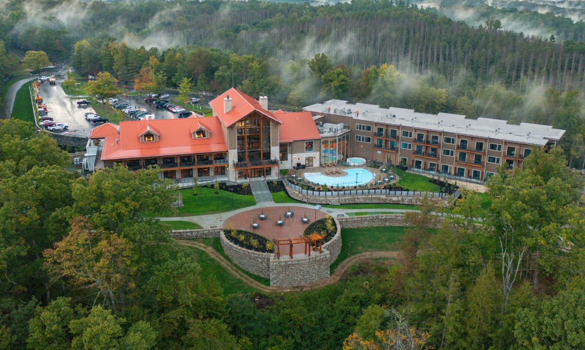 An aerial view of Hocking Hills Lodge & Conference Center in Ohio, surrounded by lush forest and misty hills, featuring a scenic pool and outdoor seating, perfect for family vacations and nature retreats.