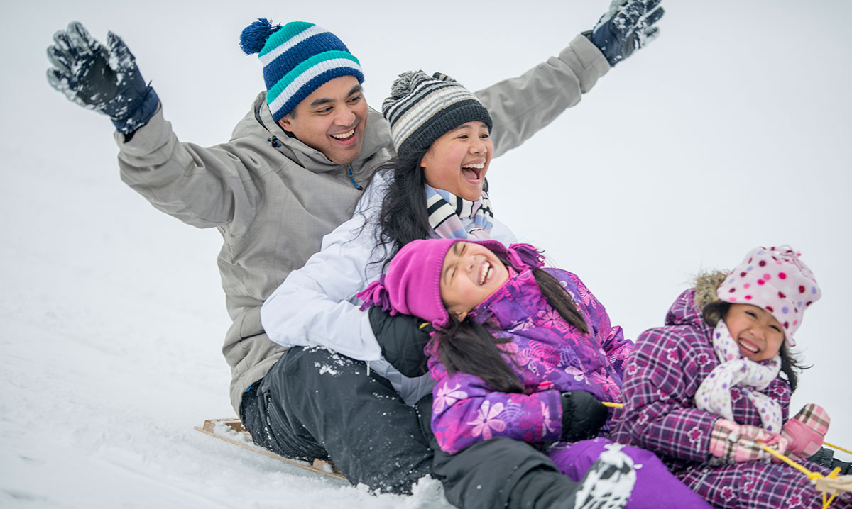 A family laughing and enjoying a thrilling sledding experience on a snowy hill, showcasing one of the best sledding hills in metro Detroit.