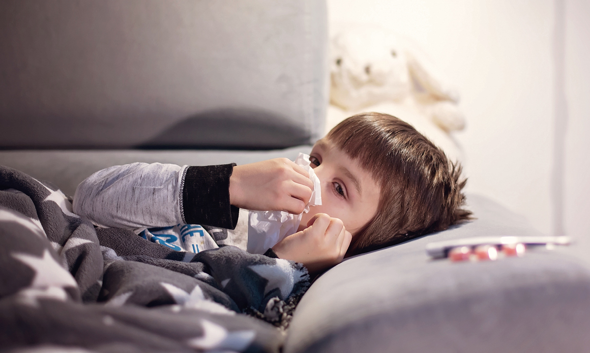 Child laying on couch blowing his nose