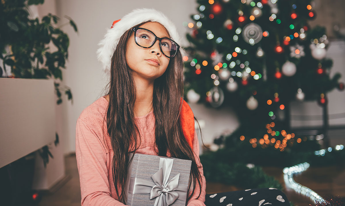 Little girl in Santa hat holding a gift and looking at the ceiling