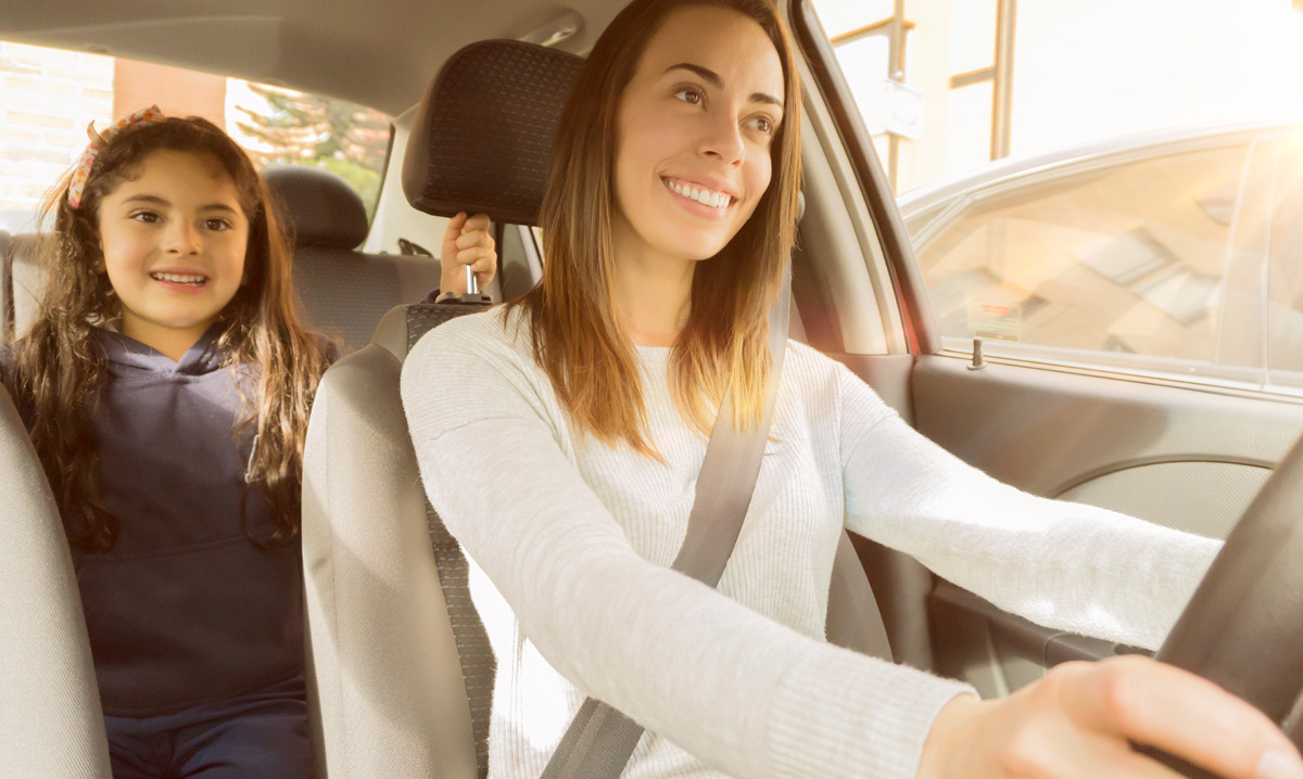 Smiling woman driving a car with a child in the backseat