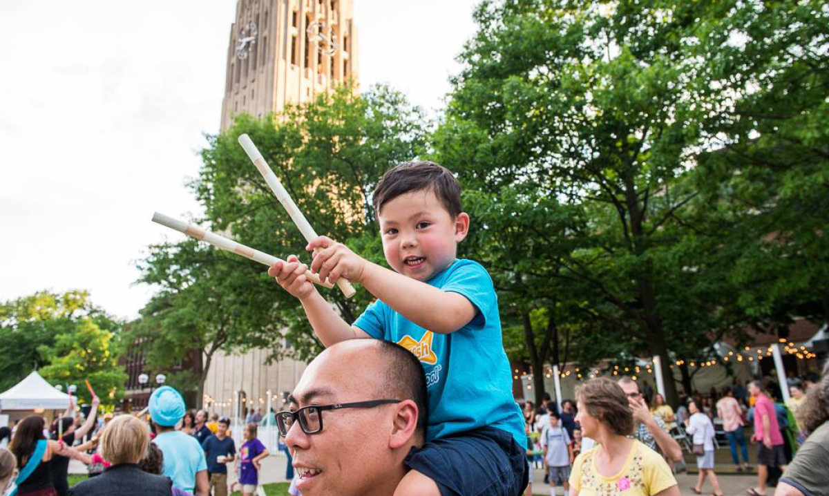 Little boy sitting on his dad's shoulders while holding sticks