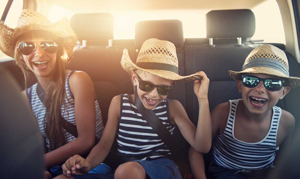 Three kids in backseat of car wearing straw hats and ready for summer fun