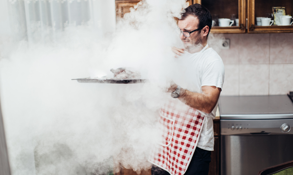 Man in apron removes smoking tray from oven