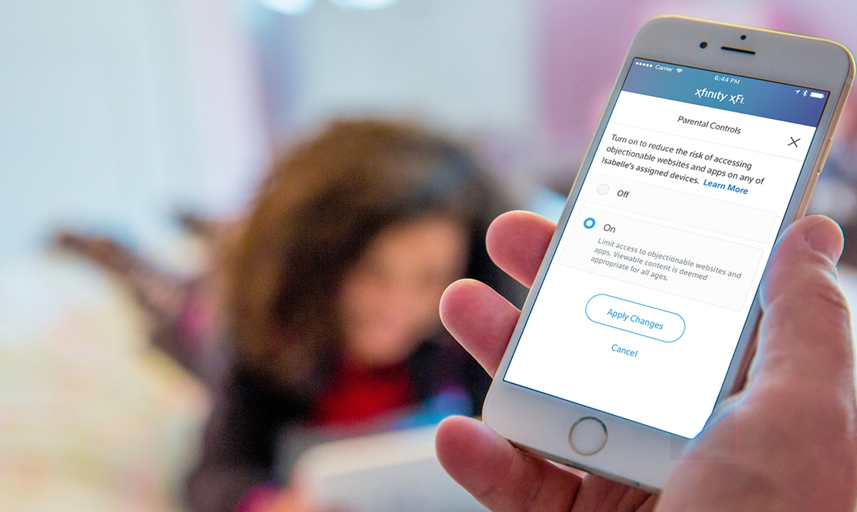 Hand holding a cell phone with a person lying down in the background