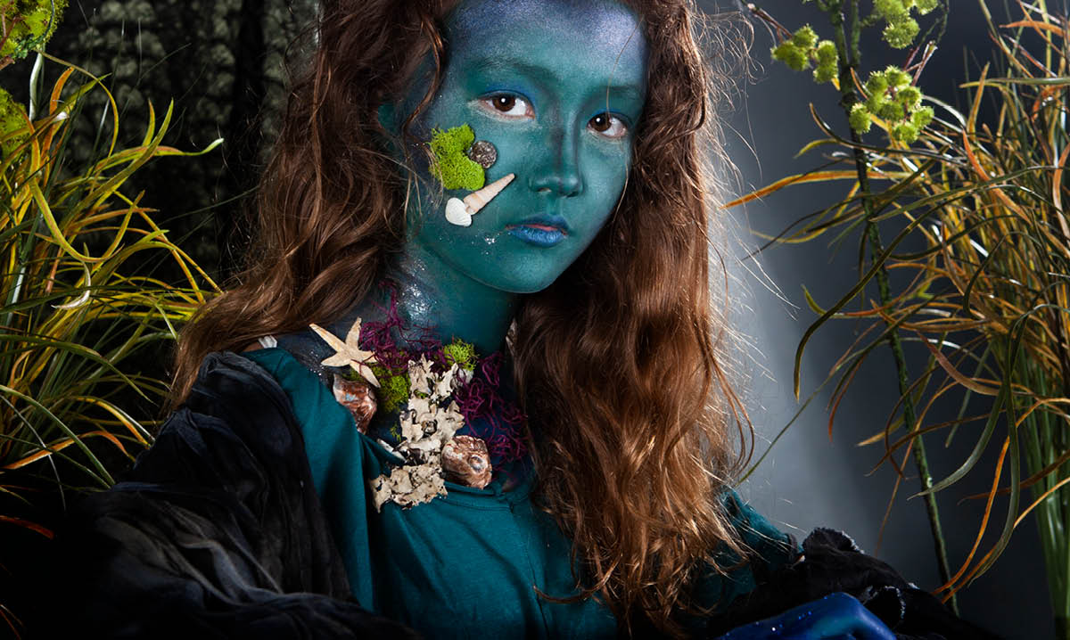 Girl in mermaid paint surrounded by leaves