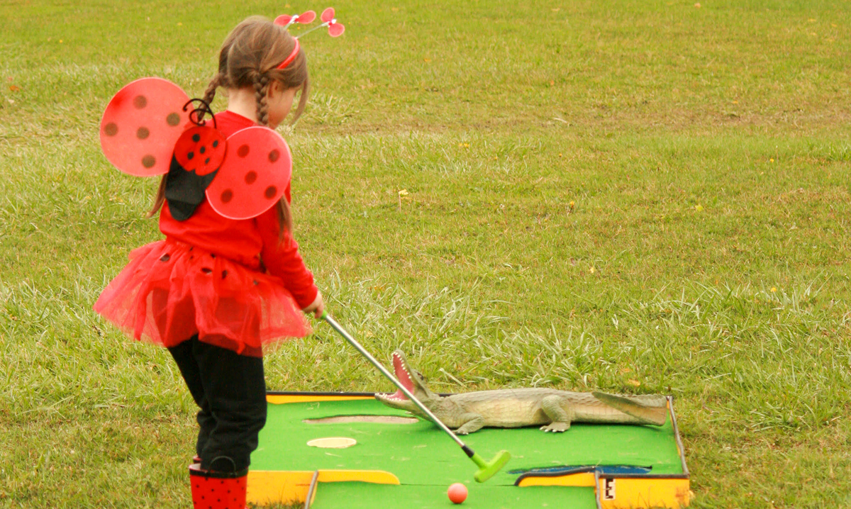 Little girl in lady bug costume playing mini golf