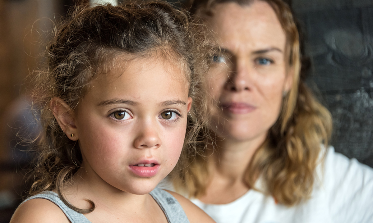 Little girl stares worried into camera with a woman behind her