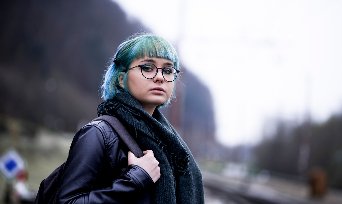 Girl with blue hair looking toward the camera with a shadowy background