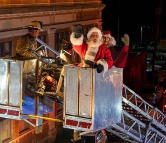 Santa waves from a firetruck lift during the Holly Dickens Festival lighted parade creating a festive holiday moment for families