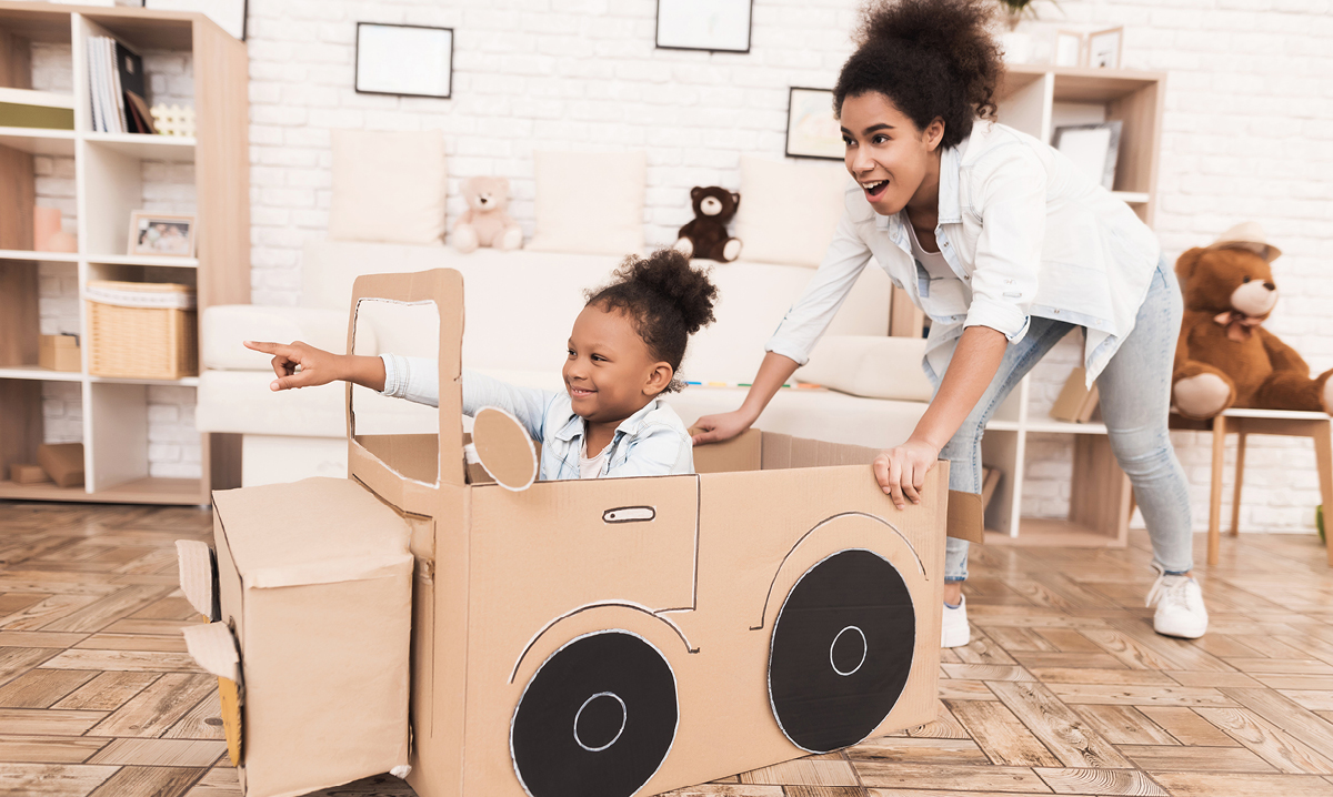 Woman pushing little girl in cardboard car