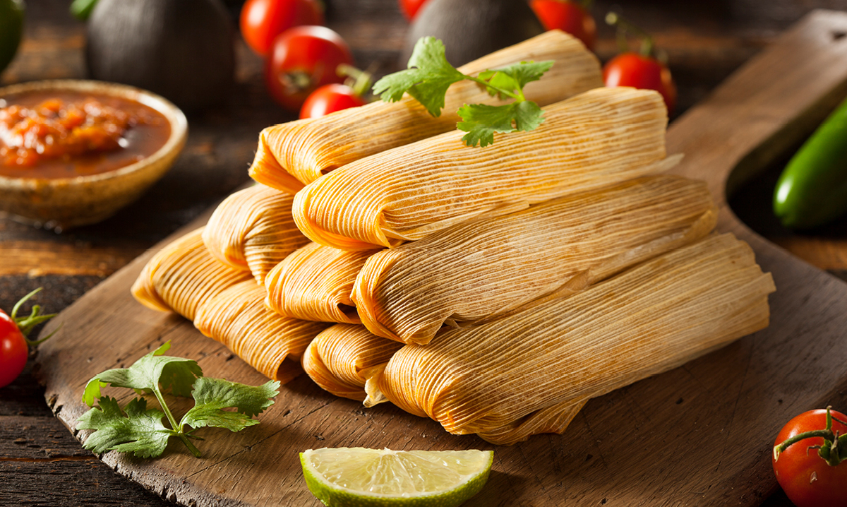 Nine tamales surrounded by tomatoes and lime