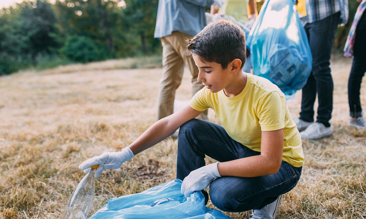 Tween boy picking up trash on sandy beach