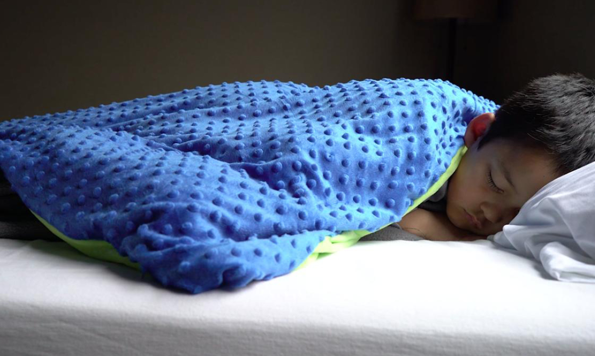 A young child sleeping under a blue weighted blanket