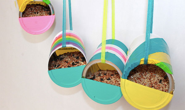 Four recycled can bird feeders hanging in front of a white background