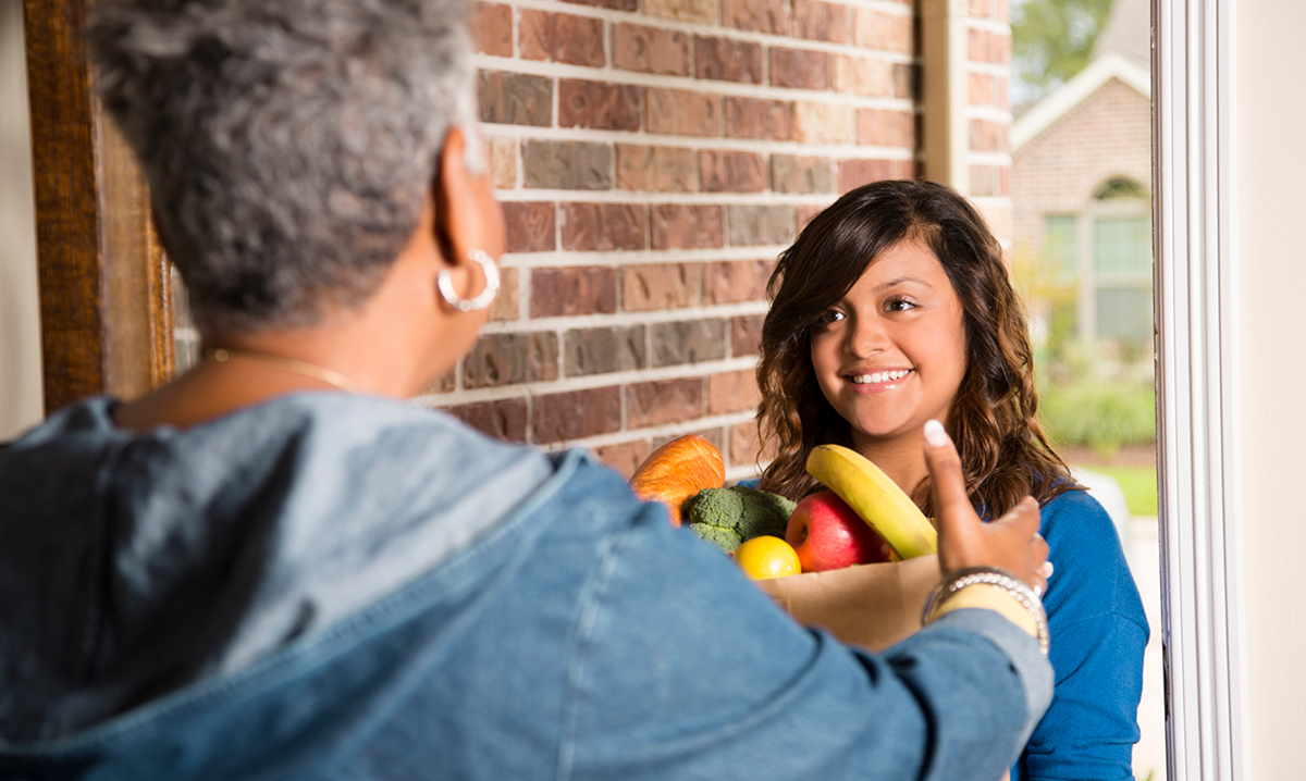 A helper brings produce groceries to an older woman's home