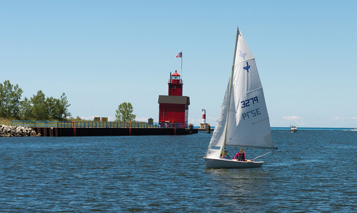 A sailboat goes past a red lighthouse on Lake Michigan