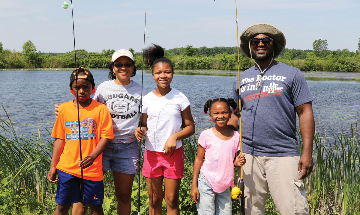 A black family of five with fishing rods near a marsh in summer