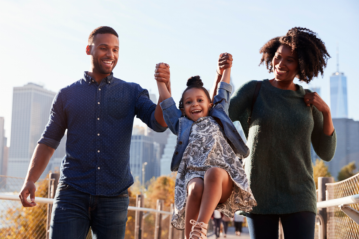 A black mom and dad lifting up their toddler daughter on vacation