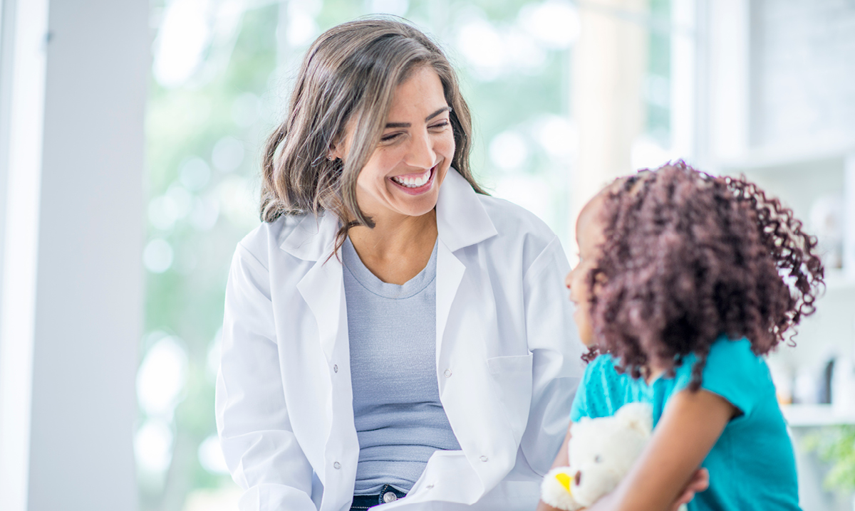 A female medical expert with a young girl holding a teddy bear