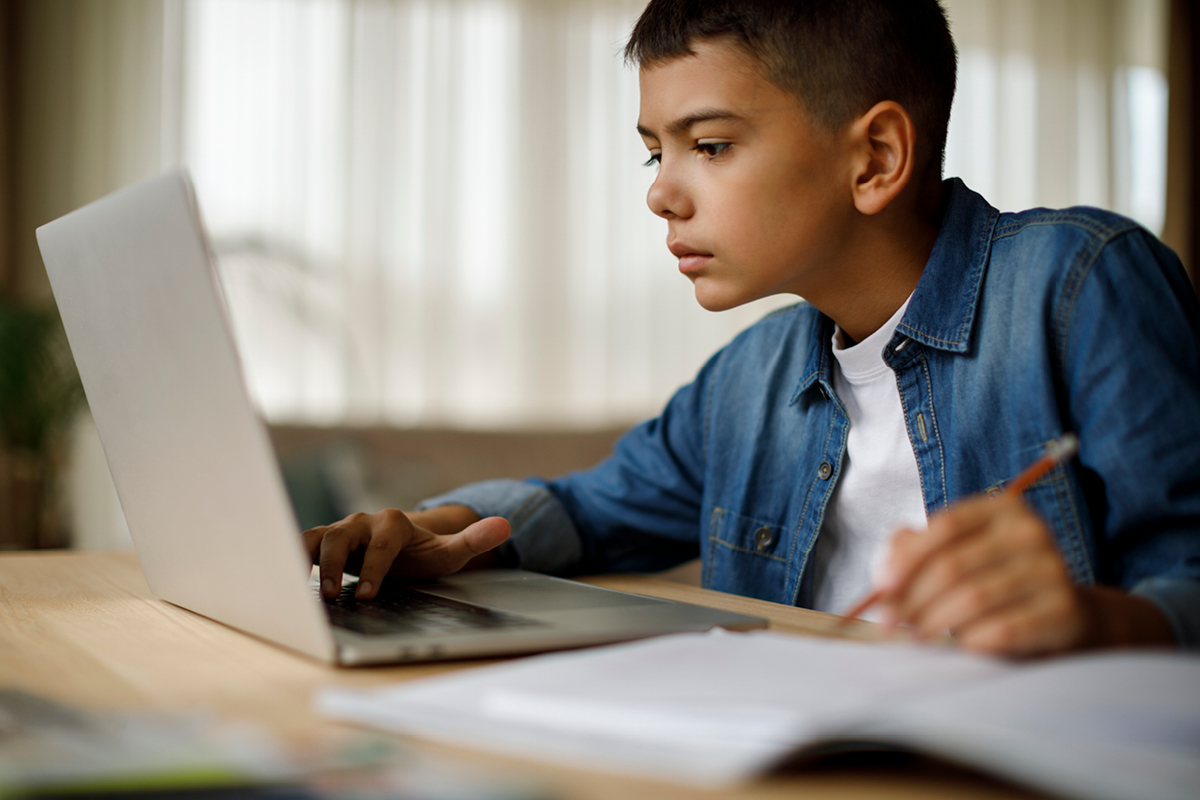 A teen boy studies for school on his laptop