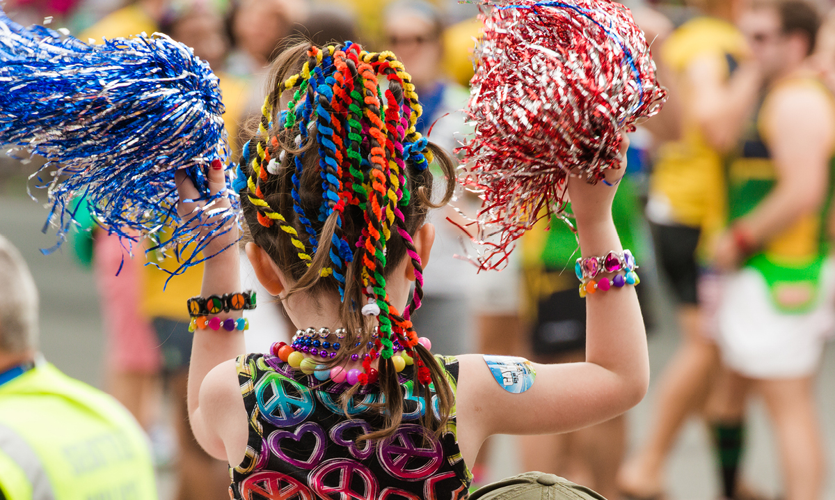 Girl in rainbow shirt, with pom poms at pride celebration