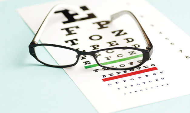 Pair of glasses on top of an eye exam chart on a light blue background