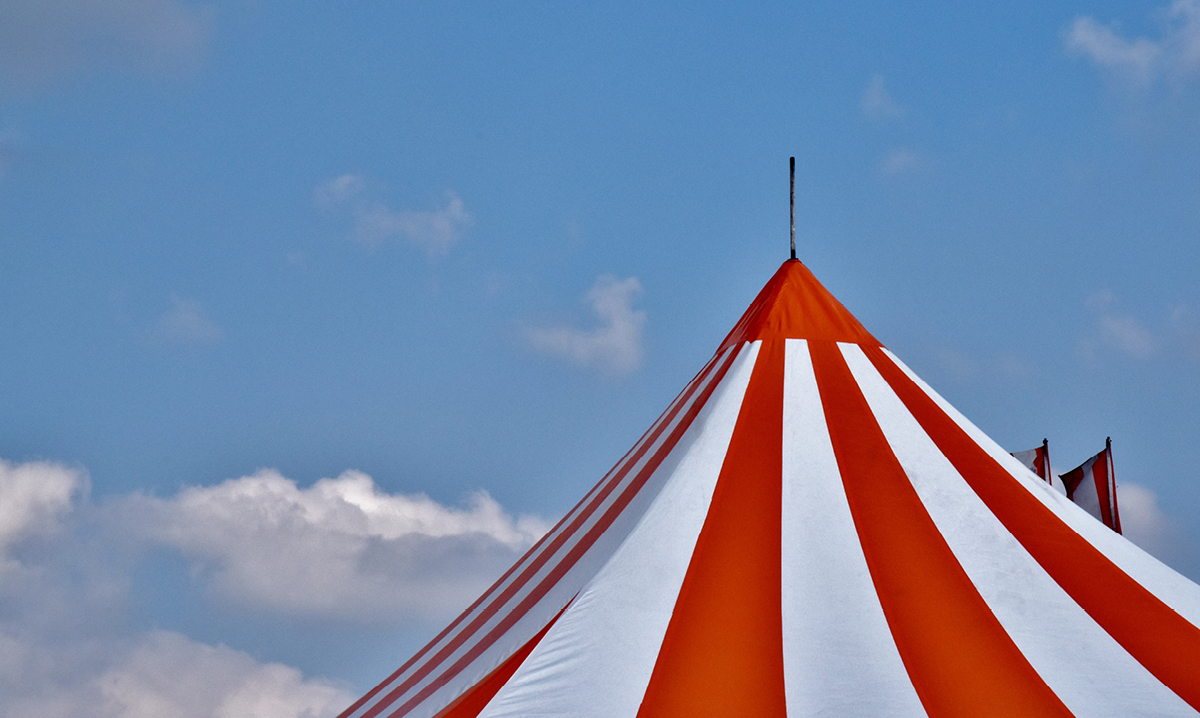Top of a red and white carnival tent against a blue sky
