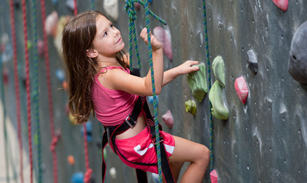 Little girl in pink on a rock climbing wall