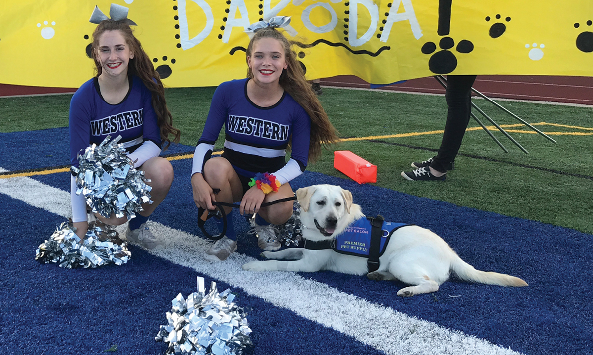 Dakota the therapy dog sitting with two cheerleaders