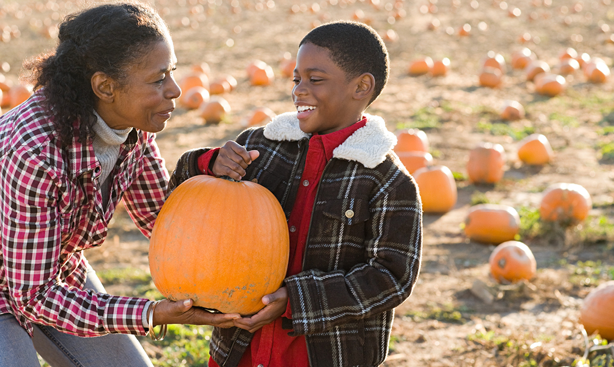 Grandma gives little boy a pumpkin. A pumpkin patch in the background