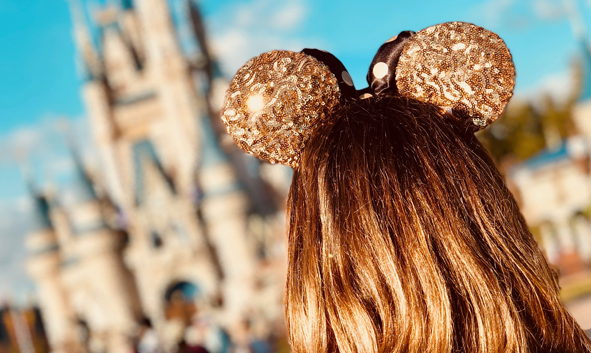 Girl wearing sparkly mickey ears in front of the disney castle