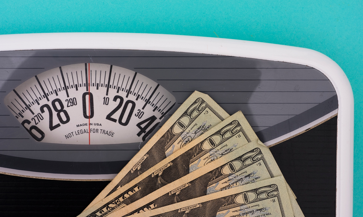 Money on top of a scale on a teal background