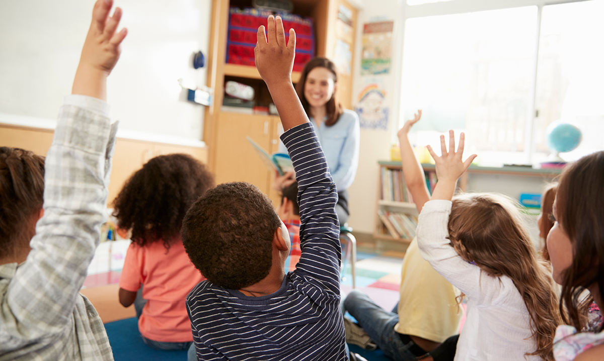 Kids raising their hands at a teacher in the background