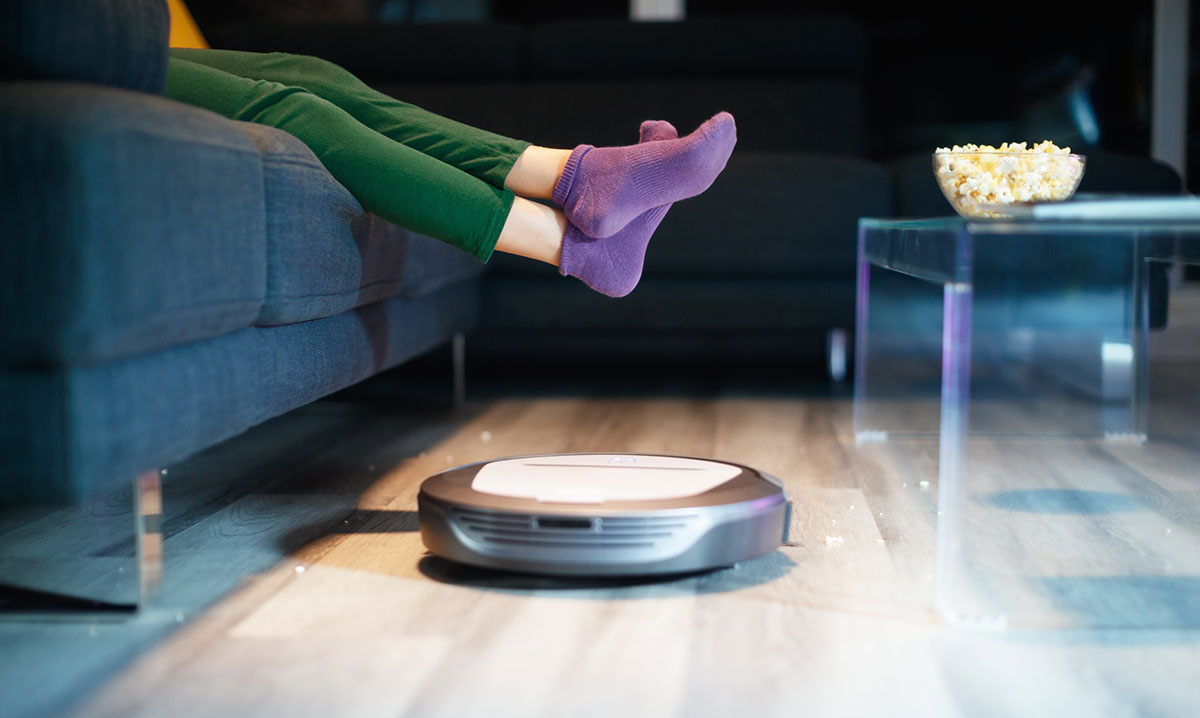 A robot vacuum cleaners rolling under a person's feet in purple socks