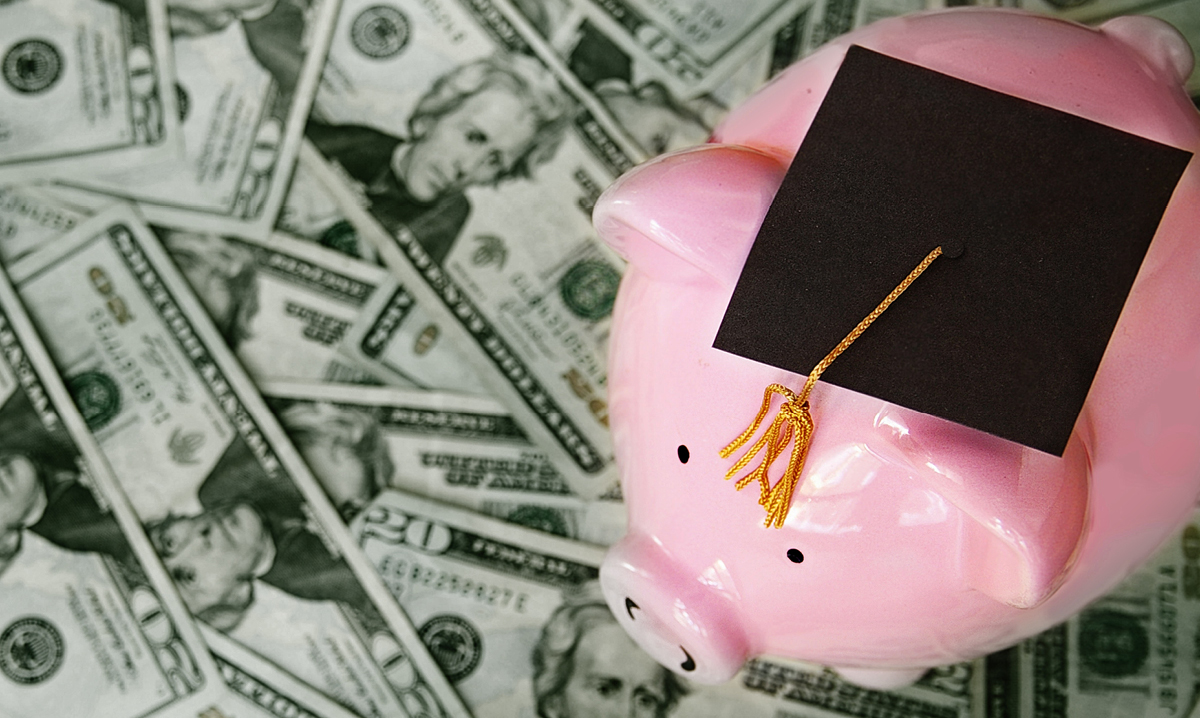 A piggy bank in a graduation hat on a pile of money