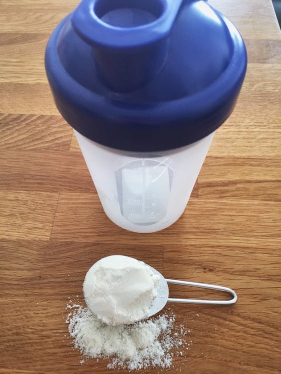 A shaker and measured protein powder on a wood table