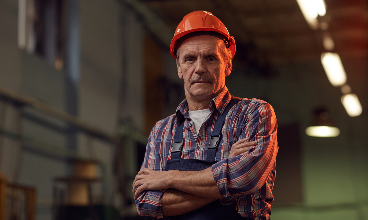 Elderly man in construction hat in factory