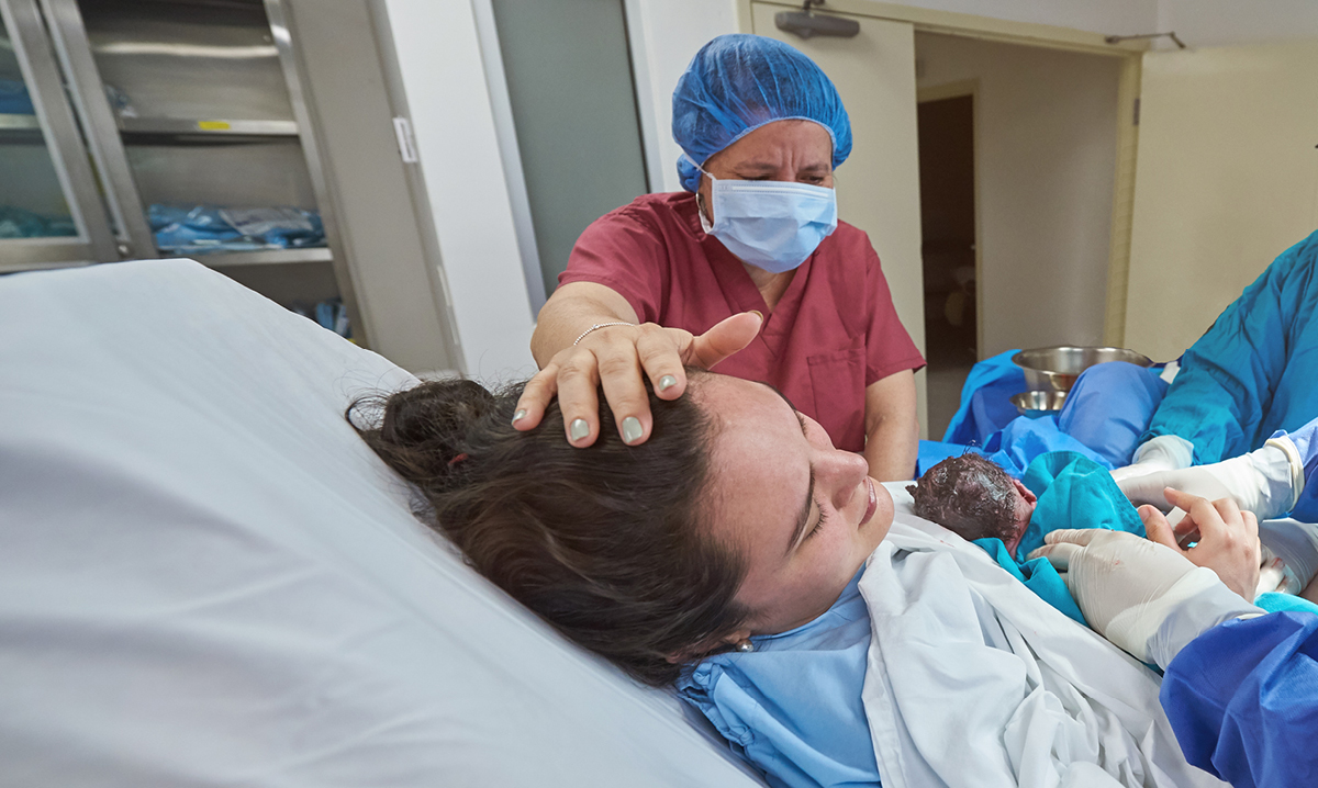 Woman in hospital gown holding newborn baby