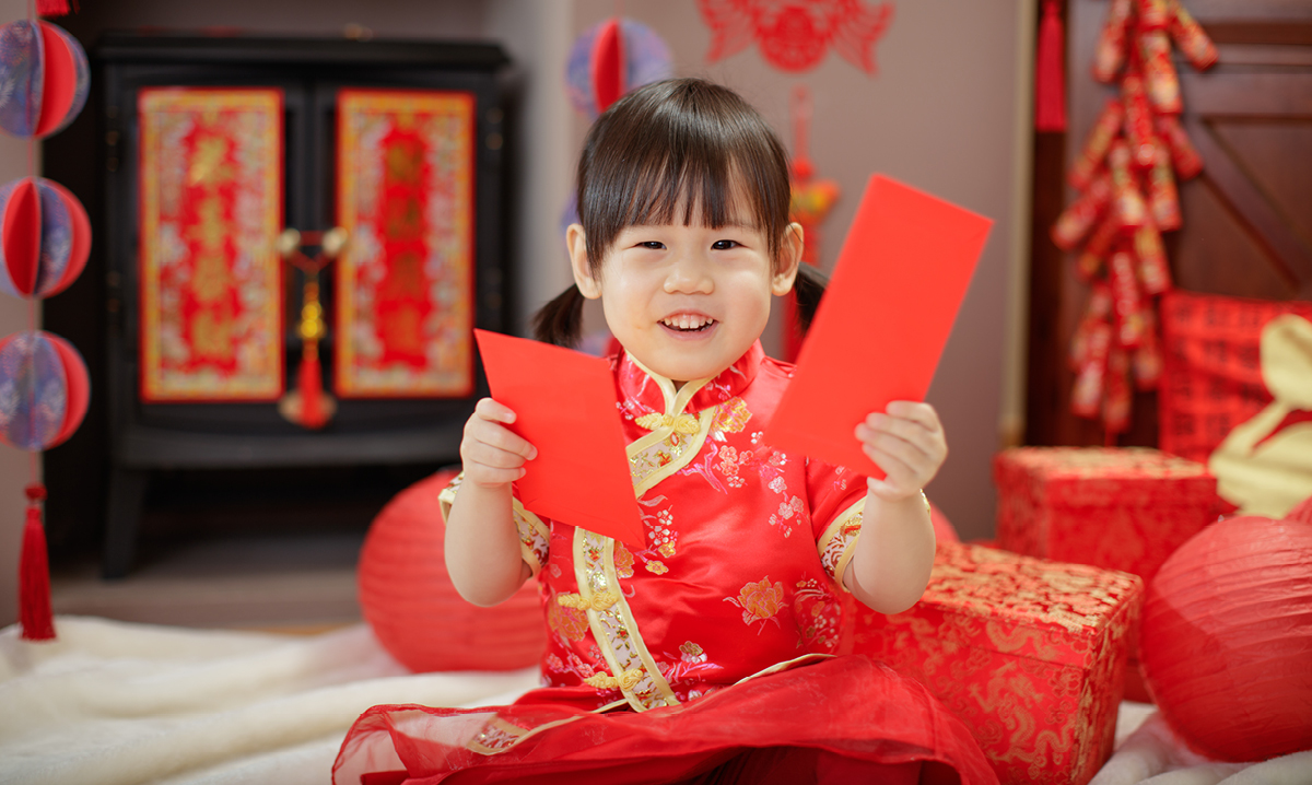 Little girl in traditional Chinese dress holding up red pieces of paper