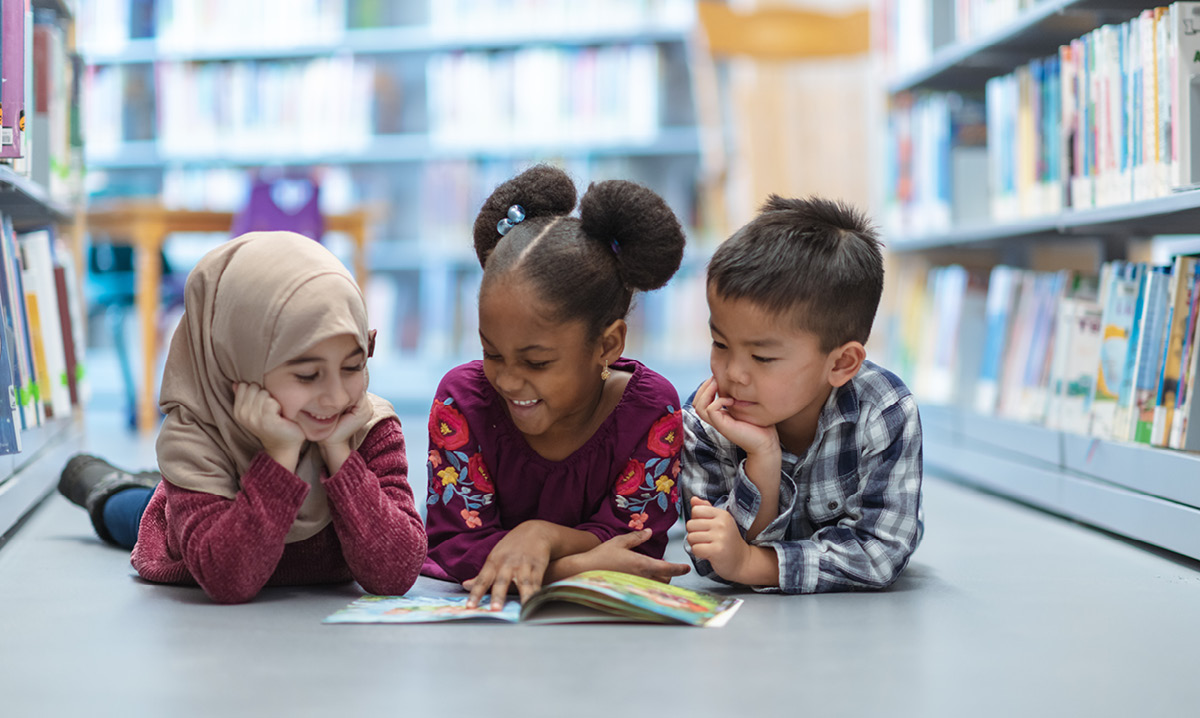 Three kids reading together on a library floor