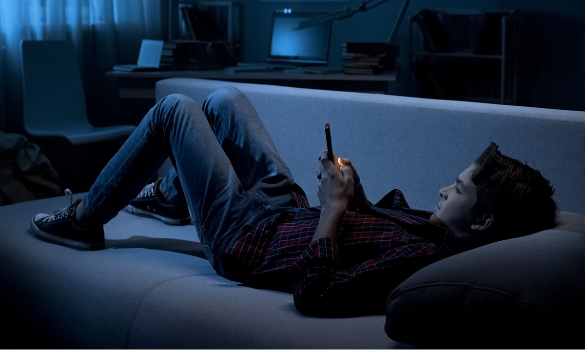 Child laying on a couch in the dark while on a phone