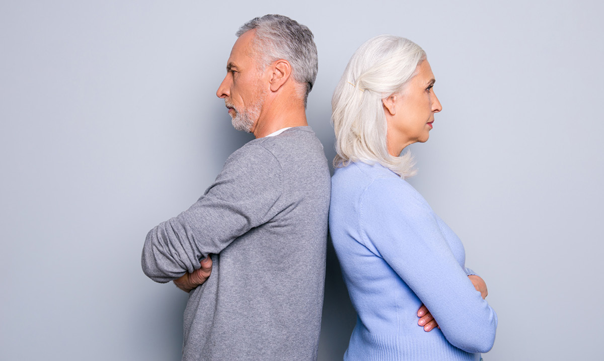 Older man and woman stand back-to-back with arms crossed