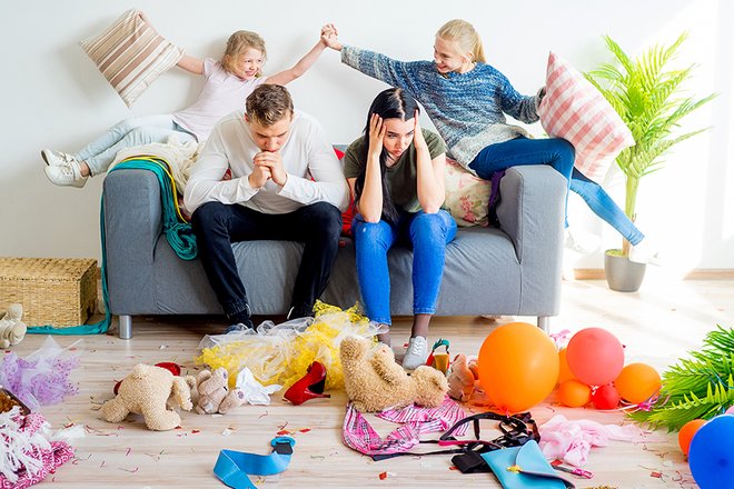Parents looking stressed surrounded by mess and misbehaving kids