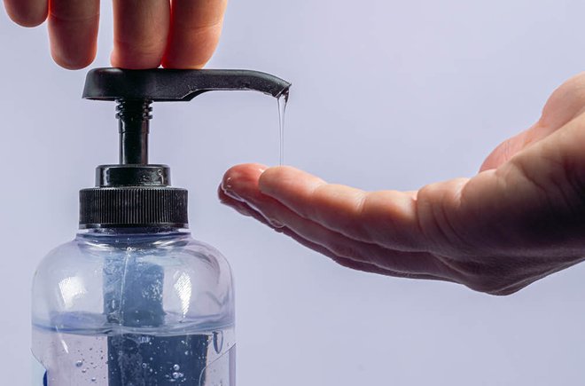 Two hands getting hand sanitizer out of a jug