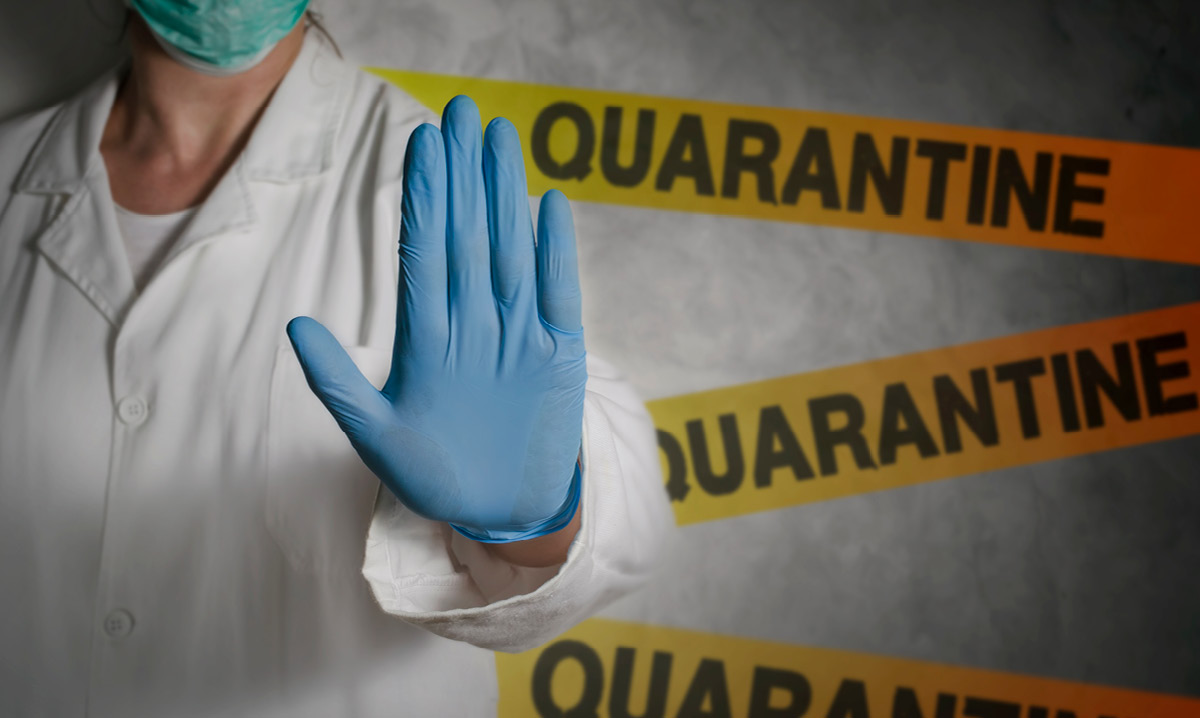 Person in doctor's scrubs holding up a gloved hand in front of three quarantine signs