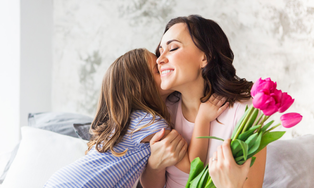 A child hugging a woman who is holding flowers