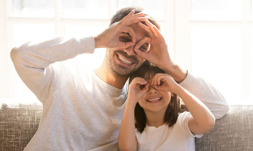 Pretty family father adorable daughter sitting on sofa do funny faces making with fingers eyewear shape like glasses looking through binoculars