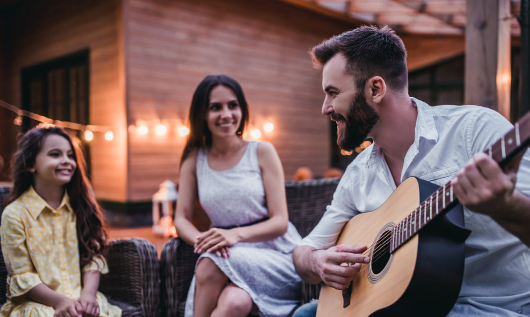 A man playing the guitar for a woman and little girl